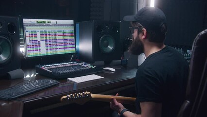 Audio engineer, musician plays electric guitar, records tune for creating new song. Computer screen showing DAW program interface with sound tracks. Work in sound recording studio. Music production.