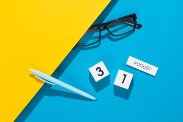 White cube calendar with the date august 31 with stationery, or office accessories on a blue yellow background. Deadline, planning, business concept