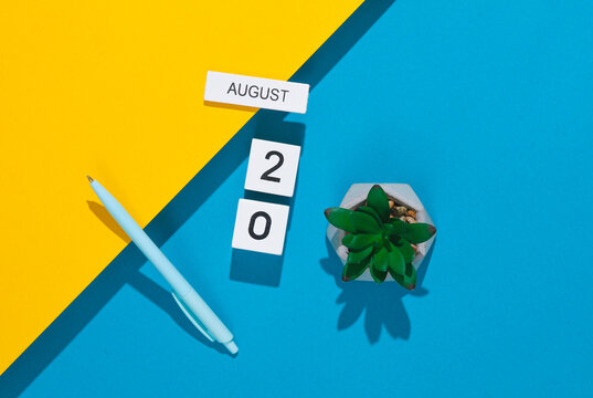 White cube calendar with the date august 20 with stationery, or office accessories on a blue yellow background. Deadline, planning, business concept