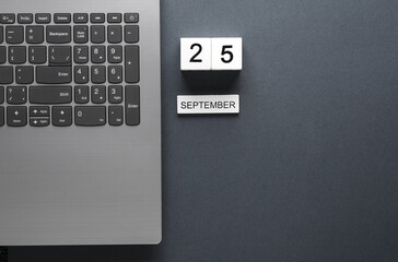 White wooden block calendar with date september 25 and laptop on gray background. Business,...