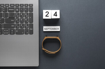 White wooden block calendar with date september 24 and laptop with smart bracelet on gray background. Business, deadline, planning, Flat lay