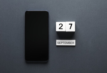 White wooden block calendar with date september 27 and smartphone on gray background. Business, deadline, planning