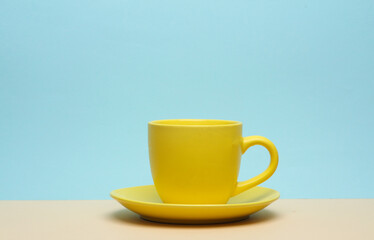 Yellow ceramic cup and saucer on a blue-beige background