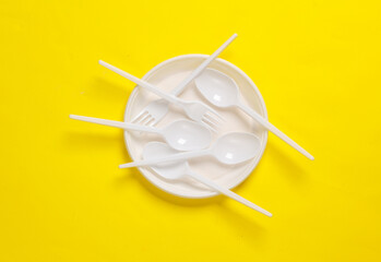 Plastic spoons and forks in a plate on a yellow background.