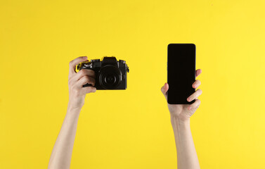 Woman's hand holding modern digital camera and smartphone on a yellow background