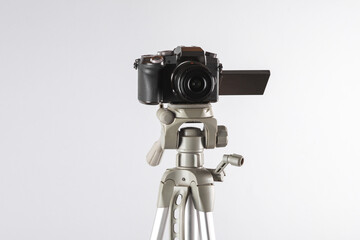 Modern digital camera with flip screen on tripod, gray background