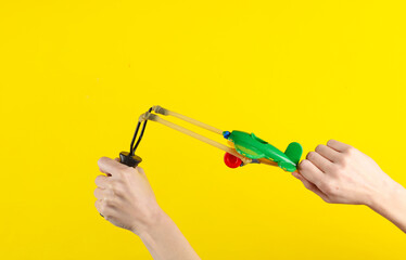 Hands holding slingshot with toy air plane on a yellow background