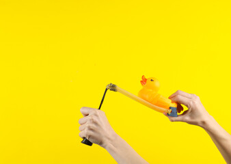 Hands holding slingshot with rubber duck on a yellow background