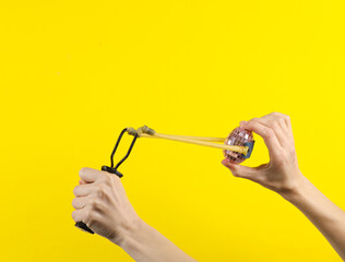 Hands holding slingshot with mirror egg on a yellow background