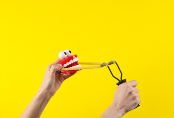 Hands holding slingshot with joke jaw on a yellow background.