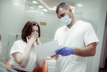 Obraz premium Professional doctor dentist showing a picture of teeth to a terrified woman patient