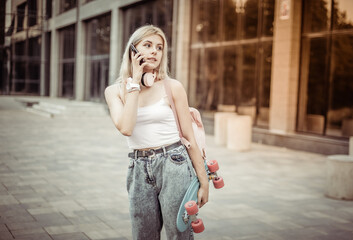 Cool young girl with skateboard talking on phone in the city