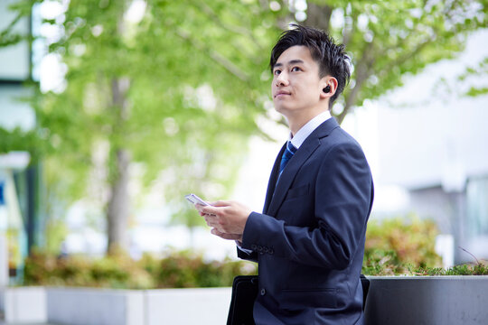 20代日本人大学生がワイヤレスイヤホンとスマートフォンを使用して就職活動をしている春のイメージ