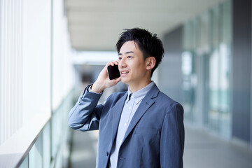 20代日本人ビジネスマンがスマートフォンを使用して仕事をしている春のイメージ