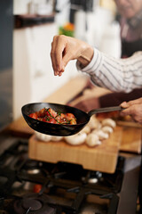 Hand, cooking and seasoning with a chef in the kitchen for meal preparation in a home for dinner. Healthy, diet and nutrition with food in a pan for wellness, hunger or satisfaction in a house