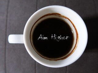 Coffee in a cup with text AIM HIGHER ,concept of decision making to work harder, try new things, chase dreams through thick and thin until getting to the top.