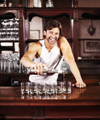 Portrait, whisky and alcohol with a handsome barman behind the counter of a pub to serve drinks during happy hour. Smile, glass and drink with a man bartender pouring a whiskey beverage in a bar