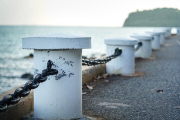 Roadside iron chain and cement pillar fence at the edge of bay route with beautiful island view. Transportation structure with nature photo, selective focus.