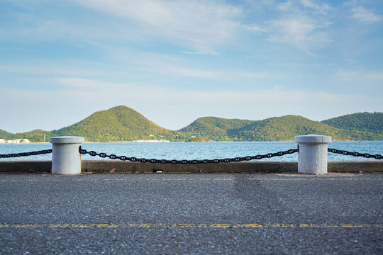 Roadside iron chain and cement pillar fence at the edge of bay route with beautiful island view. Transportation structure with nature photo, selective focus.
