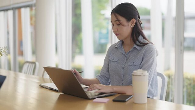 Young adult woman asia people happy work at coworking space table self study learn MBA class online course. Smart worker reskill upskill job searching data write plan on laptop. Urban modern workspace