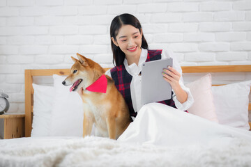 Beautiful asian woman looked content as she hold her tablet while the furry dog sat patiently...