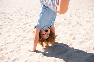 Kid jumping upside down on sand. Funny kids emotions. Outdoor close up portrait of a cute little...