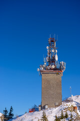 Naklejka premium Tower of telecommunication with many antennas, in a beautiful winter mountains landscape, with trees covered in snow and copy space.