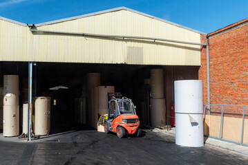 Forklift with clamps to move reels of paper in a warehouse of a paper industry.