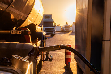 Filling the fuel tank of a truck at a gas station, with several trucks in the background. - obrazy, fototapety, plakaty