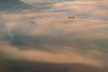 Aerial view of the valley in early morning mist, beautiful in the highlands. Low clouds and fog cover the sleeping meadow. Alpine mountain valley mists landscape at dawn. Serene moment in rural area