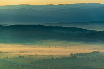 Aerial view of the valley in early morning mist, beautiful in the highlands. Low clouds and fog cover the sleeping meadow. Alpine mountain valley mists landscape at dawn. Serene moment in rural area