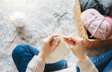 Young woman knitting warm scarf indoors