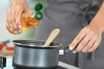 cropped image of cook pouring oil into saucepan