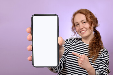 Fototapeta na wymiar cute red-haired curly woman shows close smartphone with blank white screen