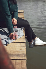Woman in white sneakers relaxing on a sunny day at the lake wooden deck.