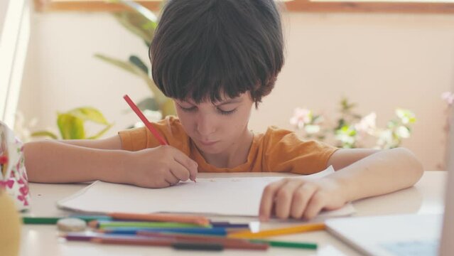 during an online drawing lesson, a boy draws in a notebook. slow motion. the child uses a laptop for learning.
