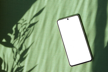 Mobile phone with empty screen mock up on green textile background with aesthetic floral sun light...