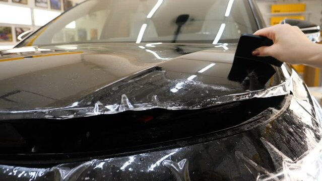 Close up to PPF installation process on a front headlight and hood. PPF is a Paint Protection Film which protect paint from scratches and stone chips. Concept of: Guard, Protect, Car, New, Work.	
