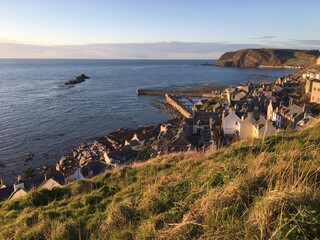View over coastal grassland to village of Gardenstown, and North Sea beyond 
