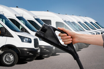 Hand with electric vehicles charging plug on a background of electric delivery vans