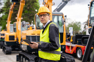 Engineer in a helmet with a digital tablet on the background of construction machine	