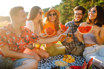 Happy groop of friend resting in nature in the picnic drinking beer, cheers. People, lifestyle, relaxation and vacations concept.