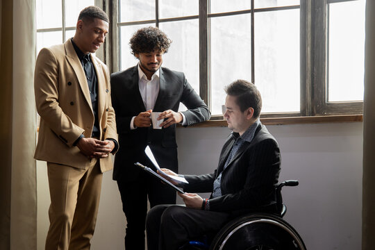 Businessman in wheelchair discussing documents with colleagues during coffee break