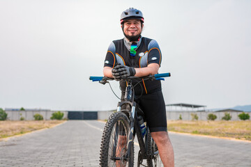 Fototapeta na wymiar Smiling cyclist on his bike in sports outfit. Chubby male cyclist in sportswear riding a bicycle outdoors