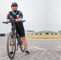 Fototapeta premium Portrait of cyclist on his bike looking at the camera with copy space. Chubby male cyclist in sportswear riding a bicycle outdoors