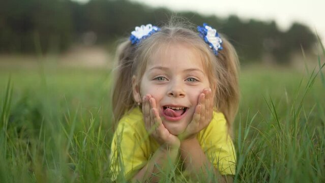 Child lies on the green grass, in the playground of nature. Little girl laughs, plays and rolls on grass. Summer vacation of child in nature outdoors. Childhood dream and freedom of travel.Child happy
