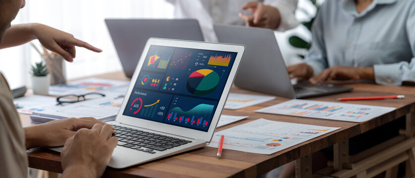 Panorama shot analyst team utilizing BI Fintech to analyze financial report with laptop. Businesspeople analyzing BI power dashboard displayed on laptop screen for business insight. Scrutinize