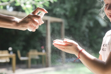 Mother applying hand sanitizer or mosquito repellent spray on her child's hand