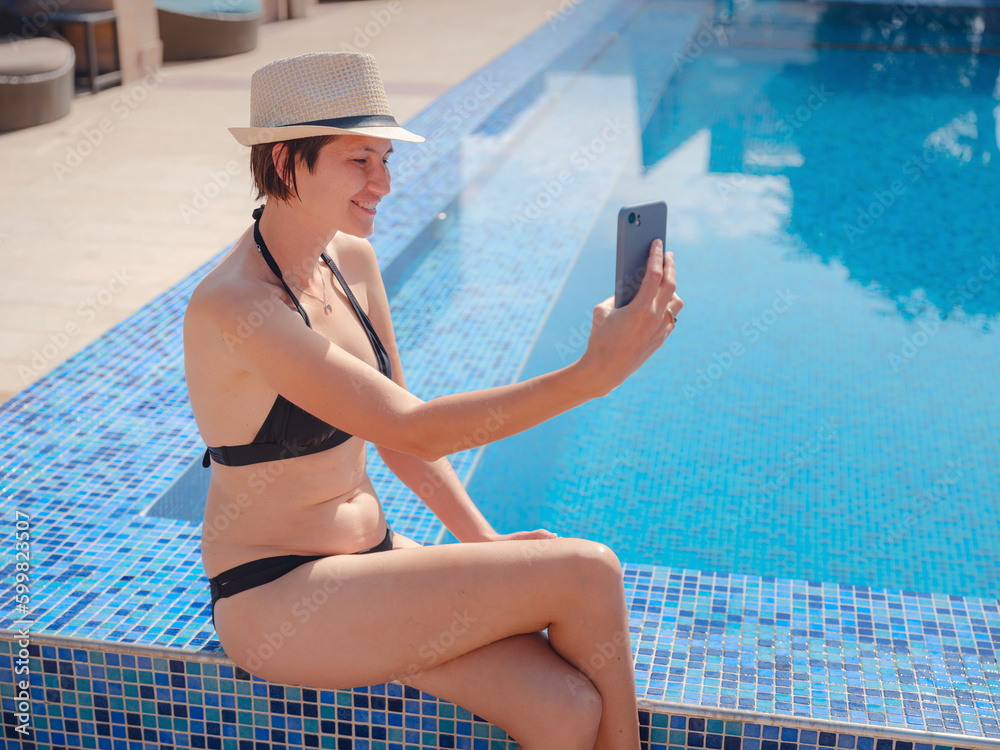 Wall mural portrait of beautiful asian woman in black swimwear and hat relaxing in swimming pool spa. hot summe