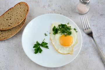 A white plate of food with a fried egg and yellow yolk and slices of bread 